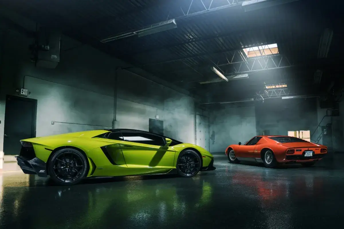 Dwa sportowe samochody, jaskrawozielony Lamborghini Aventador i pomarańczowy Lamborghini Miura, stoją w zadymionym garażu. Te zdjecia z samochodem to marzenie każdego fana motoryzacji.