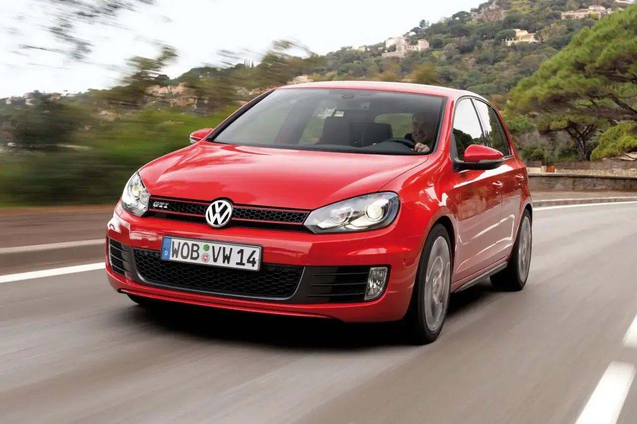 Czerwony Golf 6 GTI pędzi po krętej drodze, za kierownicą uśmiechnięty kierowca.