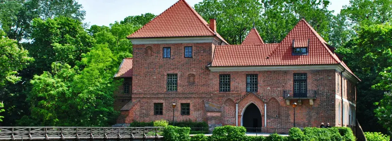 Zamek w Łęczycy, otoczony zielenią, to jedna z gł&oacute;wnych atrakcji regionu. Ceglana budowla z czerwonym dachem prezentuje się okazale.