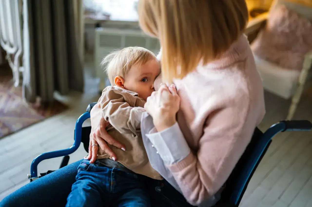 Mama w w&oacute;zku inwalidzkim karmi piersią dziecko. To ważny moment, kt&oacute;ry może być częścią procesu, jak odstawić dziecko od piersi.