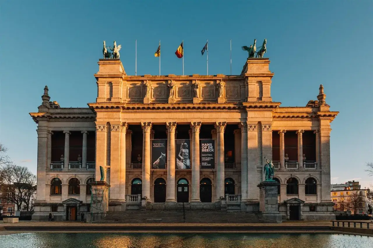Kr&oacute;lewskie Muzea Sztuk Pięknych w blasku zachodzącego słońca. Monumentalna fasada z rzeźbami i flagami.