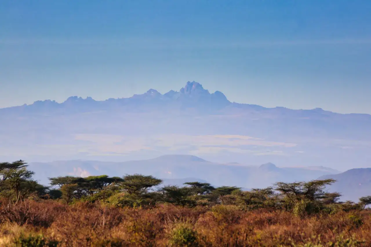 Majestatyczny Mt Kenya wyłania się z mgły nad sawanną, otoczony akacjami i suchą trawą.