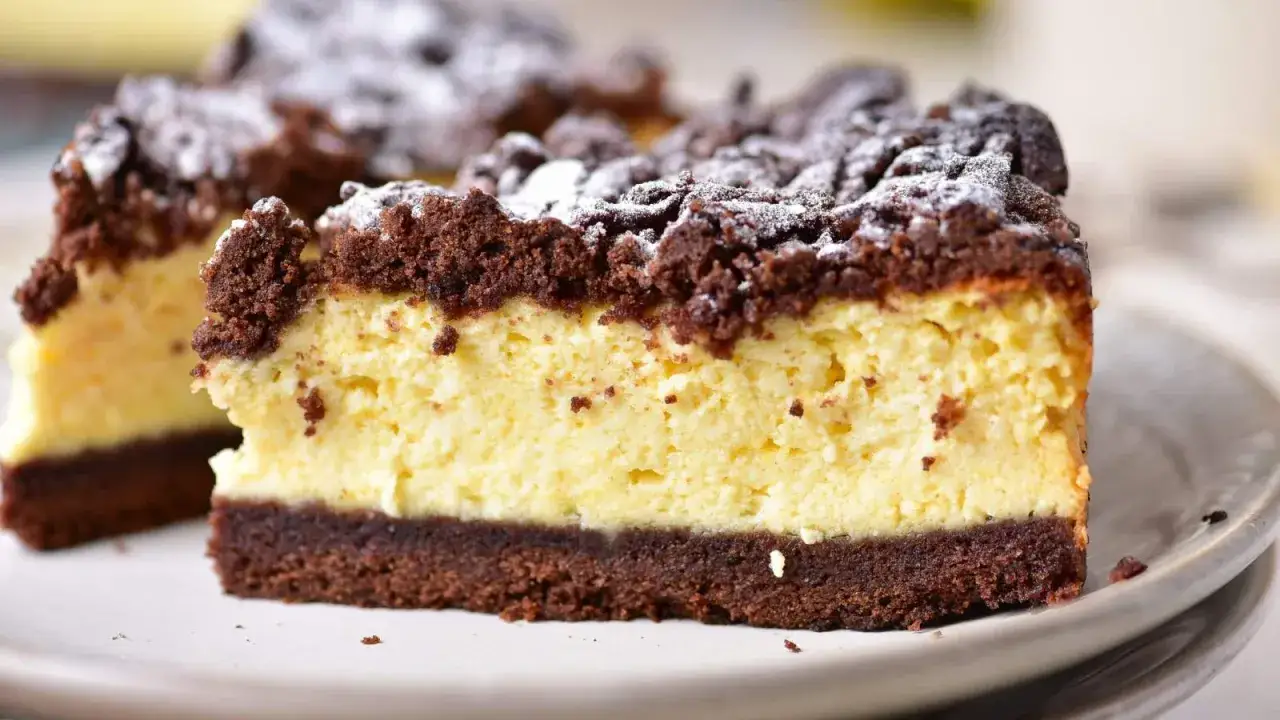 Kawałek sernika królewskiego z czekoladową kruszonką i kremowym nadzieniem, posypany cukrem pudrem. Idealny przepis na sernik królewski.
