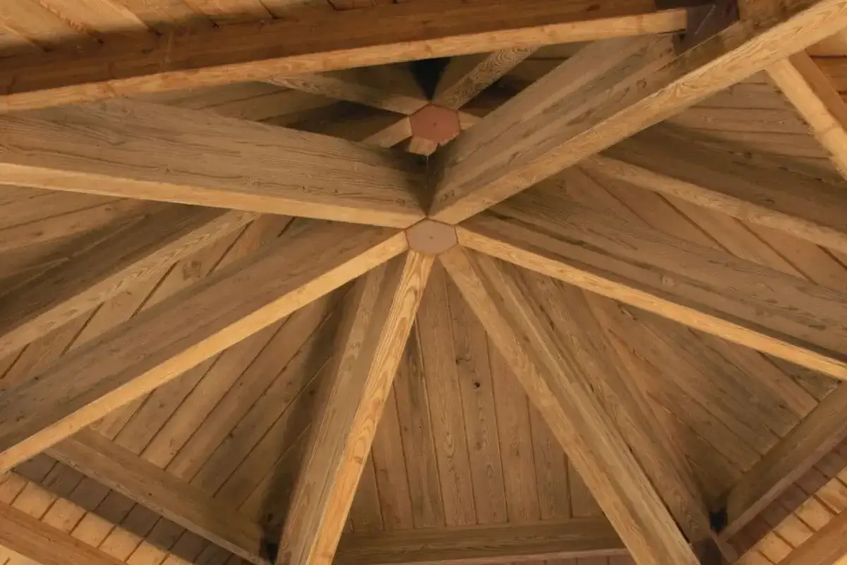 Drewniane belki tworzą skomplikowaną konstrukcję dachu altany, nadając jej solidny i naturalny wygląd.