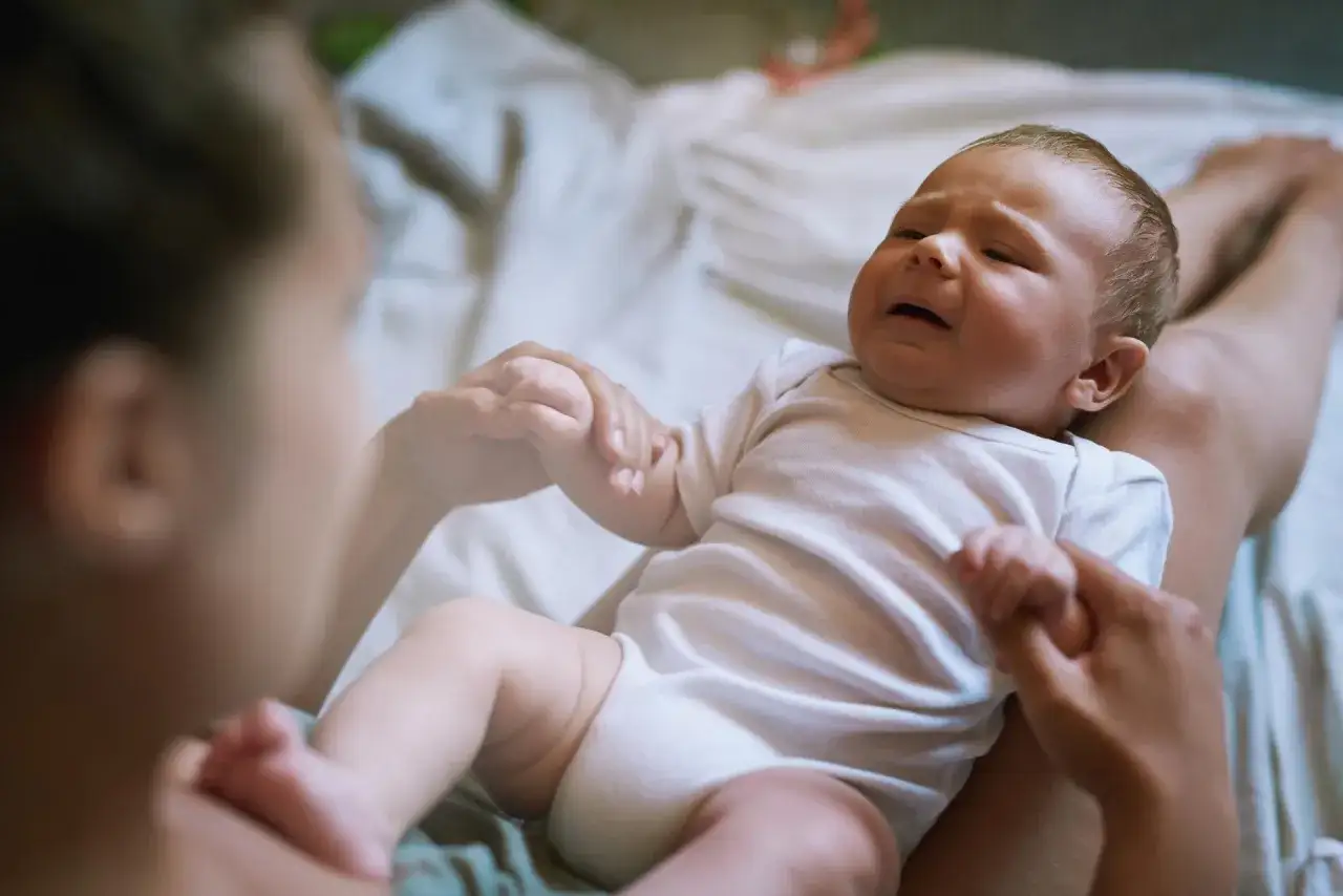 Płacz dziecka, które przechodzi pierwszy skok rozwojowy u noworodka. Mama trzyma je za rączkę, próbując uspokoić.