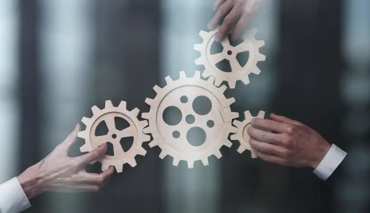 Dłonie składają drewniane tryby, symbolizując standaryzację pracy i wsp&oacute;łpracę w osiąganiu wsp&oacute;lnego celu.