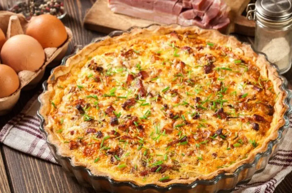 Pyszny, złocisty farsz do tarty na słono z boczkiem i szczypiorkiem, gotowy do podania. Obok jajka i składniki.