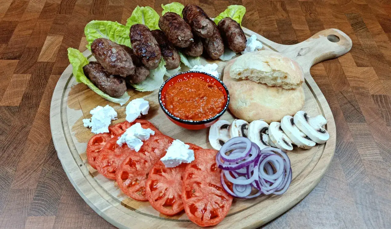 Pyszne cevapcici makłowicz na desce z pomidorami, cebulą, pieczarkami i ajwarem.