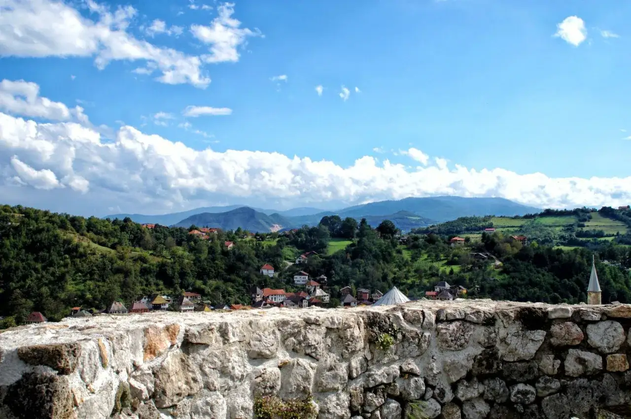 Widok na zielone wzg&oacute;rza i domy z czerwonymi dachami w Travniku, Bośnia. Kamienny mur na pierwszym planie.