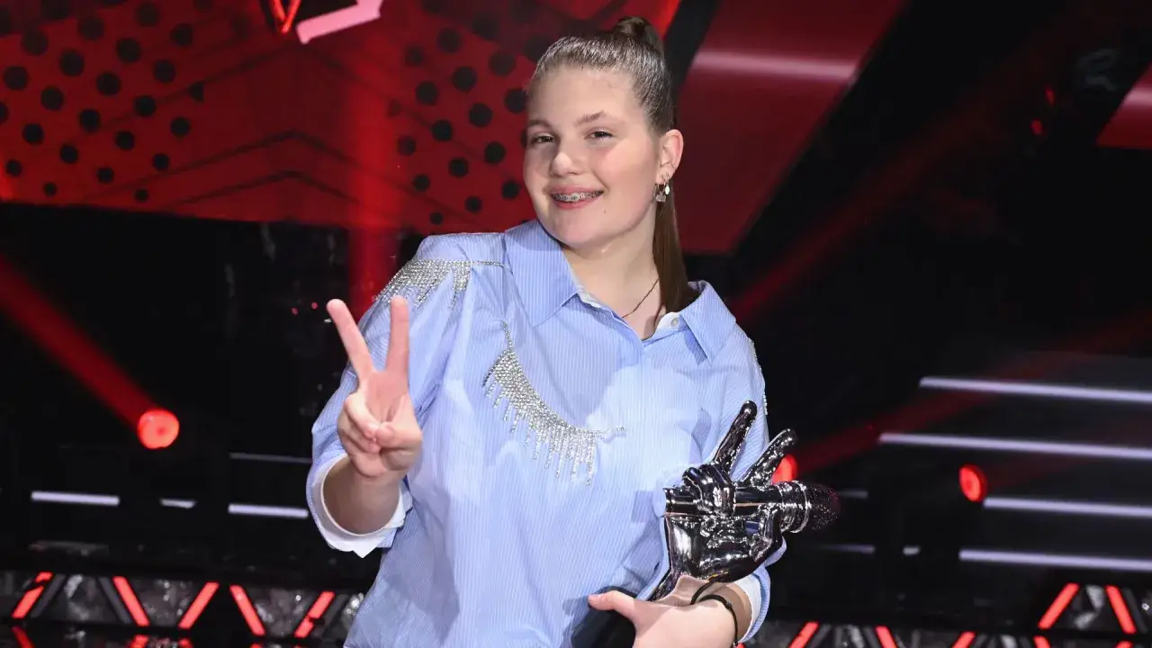 Młoda artystka z trofeum, kt&oacute;ra wygrała The Voice Kids, pokazuje znak pokoju.