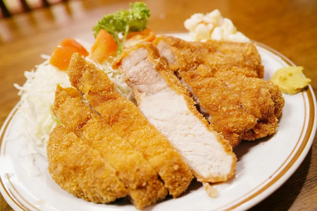 Pyszny kotlet schabowy przepis na chrupiący obiad. Podany z surówką z kapusty, pomidorkami i musztardą.