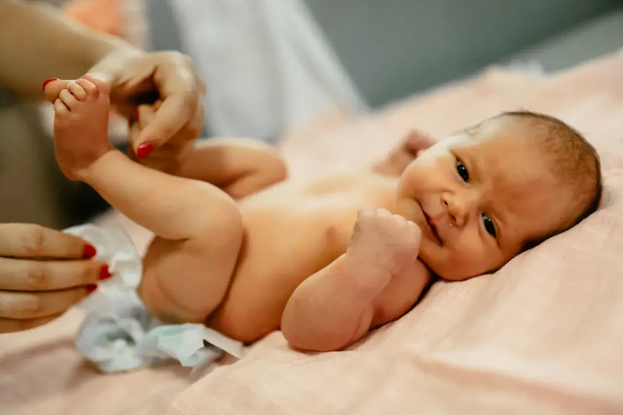 Noworodek leży na różowym kocyku, a mama zmienia mu pieluszkę. Ważne jest, co ile zmieniać pieluszkę noworodkowi.