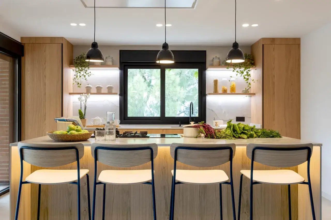 Moderna cocina con isla central de madera, taburetes y encimera con frutas y verduras.