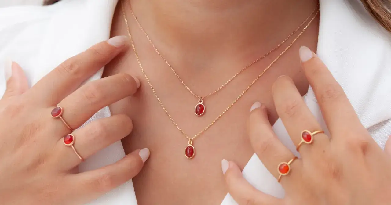 Dłonie ozdobione pierścionkami i naszyjnikami z czerwonymi kamieniami. Co oznacza diament na sympatii? To symbol odwagi i pasji.