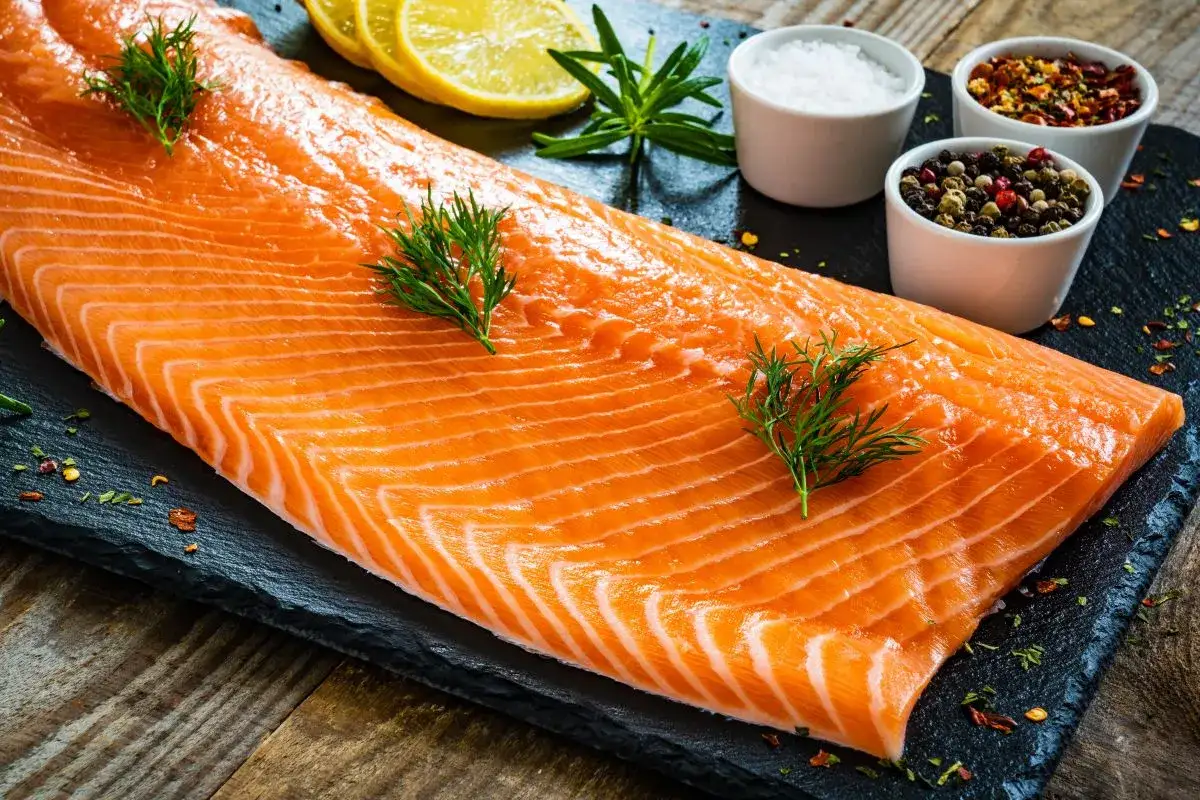 Świeży łosoś na desce z cytryną i przyprawami. Czy łososia można mrozić? Tak, aby zachować jego świeżość na dłużej.