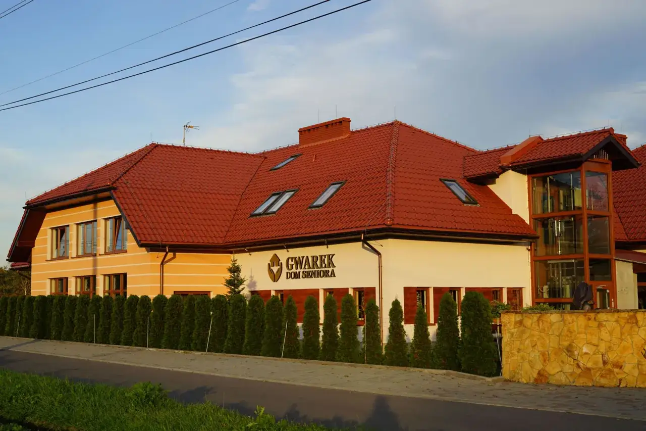 Dom Seniora Gwarek, nowoczesny budynek z czerwoną dachówką i zielonym żywopłotem.
