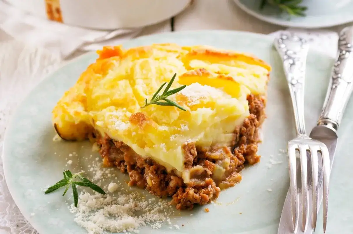 Pyszna zapiekanka pasterska (Shepherd's Pie) z warstwą mielonego mięsa i kremowym purée ziemniaczanym, ozdobiona gałązką rozmarynu.