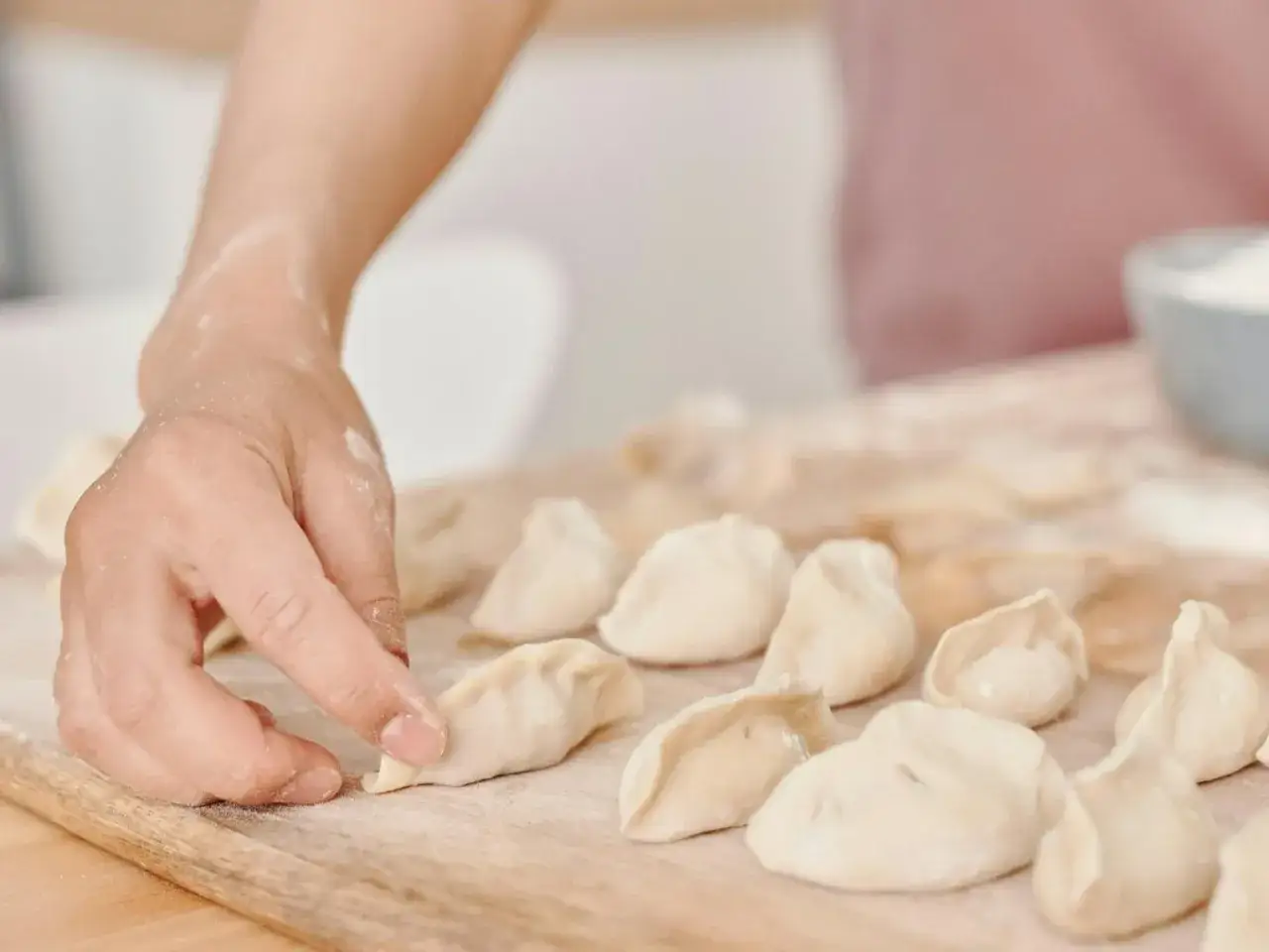 Dłoń formuje pierożki na desce. Zastanawiasz się, ile wyjdzie pierogów z pół kilograma mąki?