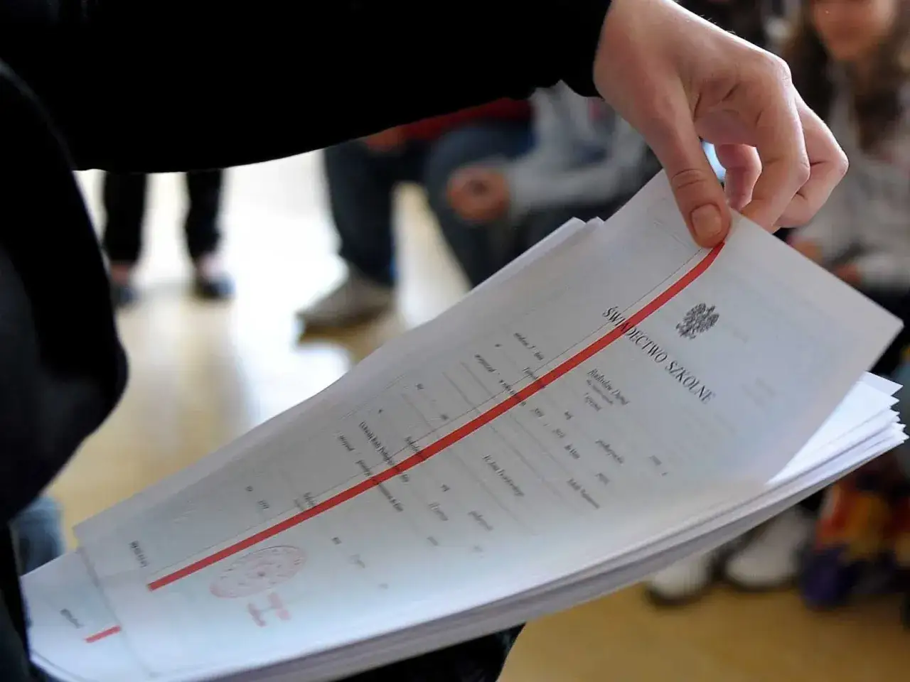 Dłoń trzyma stos świadectw szkolnych. Czy religia liczy się do średniej? To pytanie nurtuje wielu uczniów.