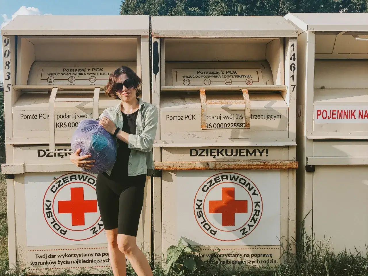 Kobieta z workiem ubrań przy kontenerze PCK. Tu można oddać ubrania dla potrzebujących.