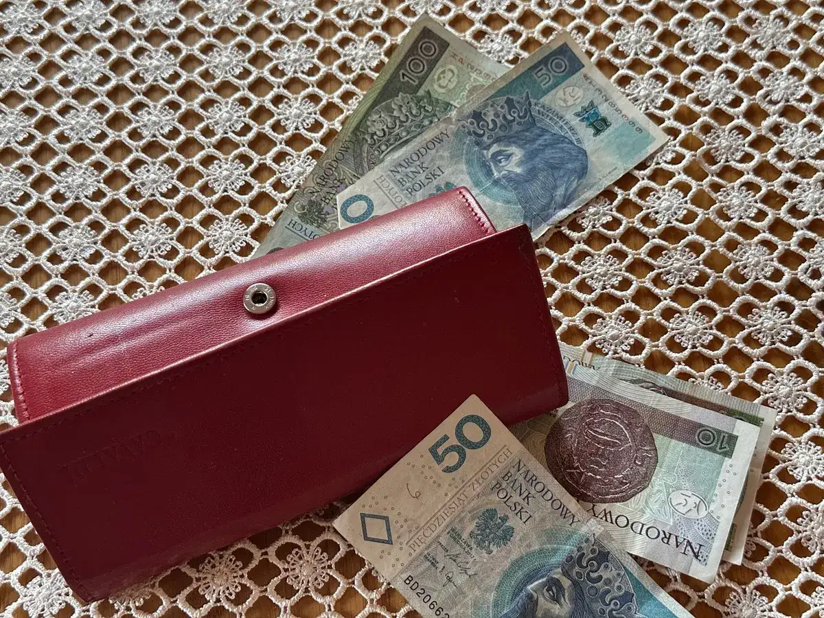 Czerwony portfel i polskie banknoty na koronkowym obrusie. Czy to wystarczy, by pokryć koszty życia, gdyby tyle wynosiła najniższa emerytura netto?