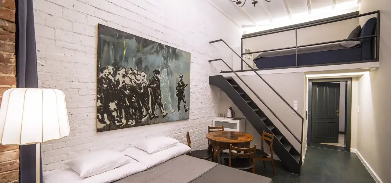 Nowoczesny pokój w hostelu z antresolą, łóżkiem, stolikiem i obrazem. To idealne miejsce dla podróżnych szukających komfortu i stylu.