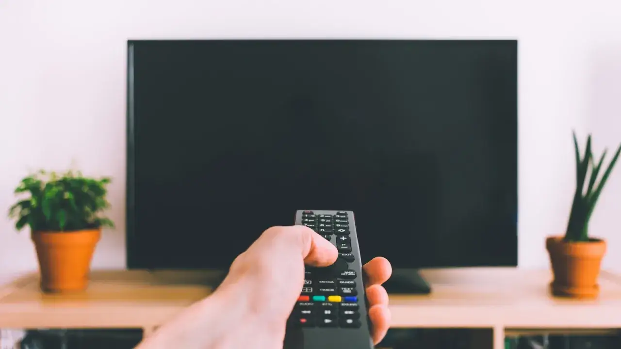 Dłoń trzyma pilot do telewizora. Zastanawiasz się, czym umyć ekran telewizora? Zadbaj o czysty obraz!