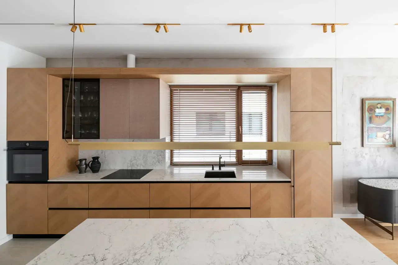 Nowoczesna kuchnia z drewnianymi frontami i marmurowym blatem. Reflektory na szynie to świetne rozwiązanie, jakie oświetlenie do kuchni wybrać.