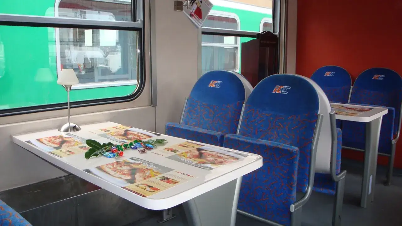 Wnętrze wagonu z niebieskimi siedzeniami i stolikiem. Czy TLK to Intercity? Tak, to wagon Intercity.