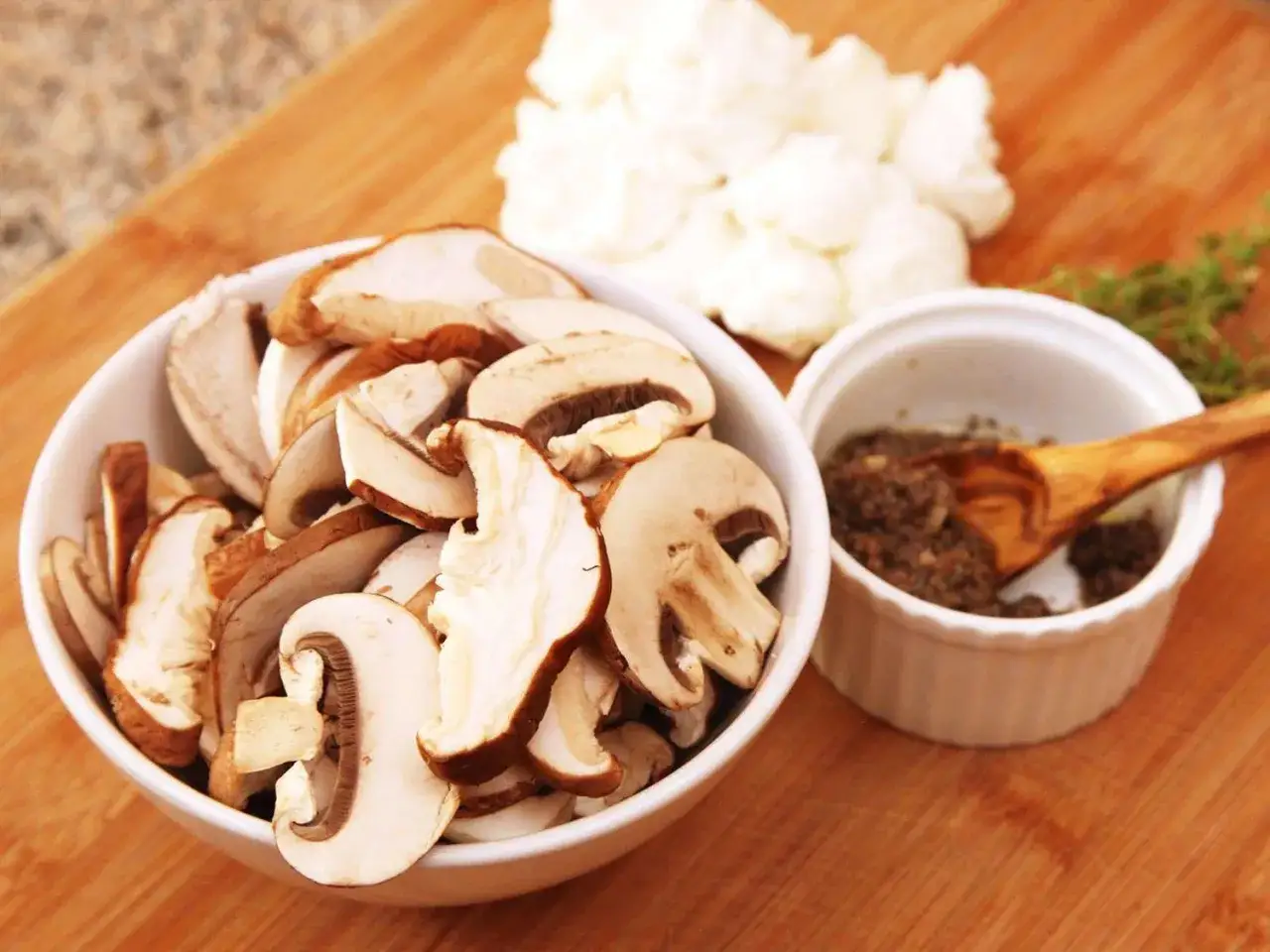 Pokrojone pieczarki do pizzy w misce, obok miseczka z pastą truflową i gałązka zi&oacute;ł.