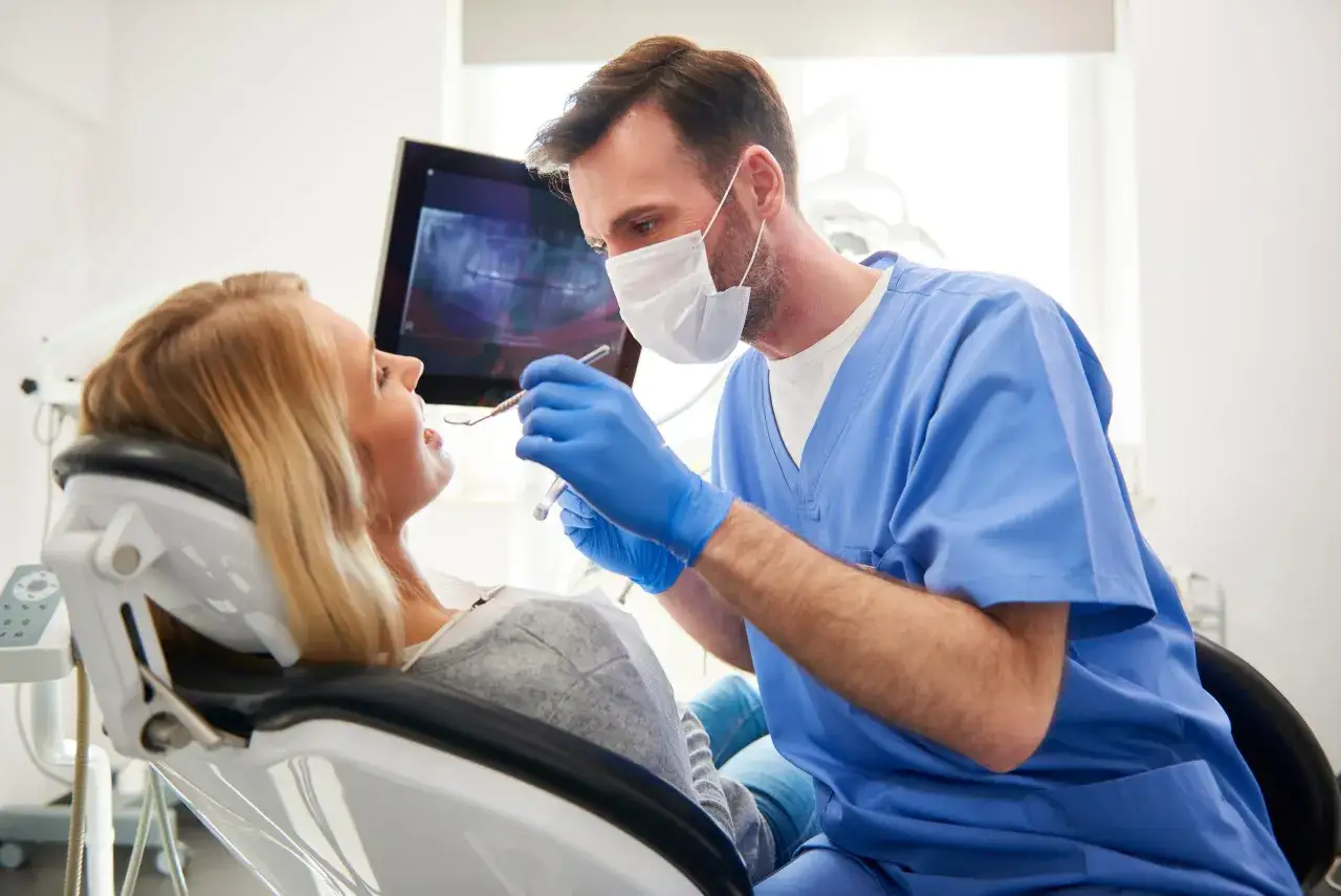 Dentysta bada pacjentkę, która martwi się krwawiącymi dziąsłami w nocy. Na ekranie widać zdjęcie rentgenowskie zębów.