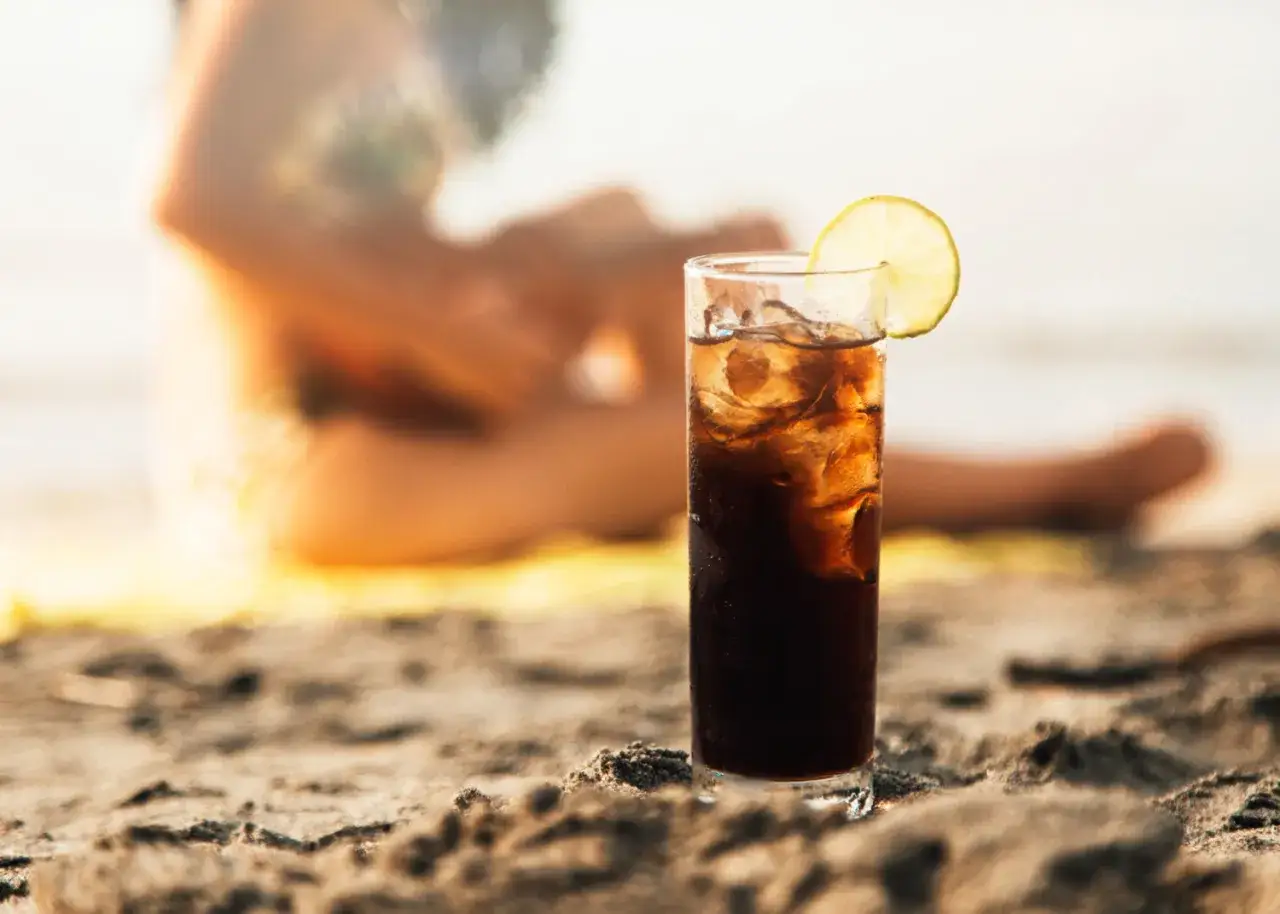 Orzeźwiający long island tea na plaży, z plasterkiem cytryny, w tle rozmyta sylwetka osoby.