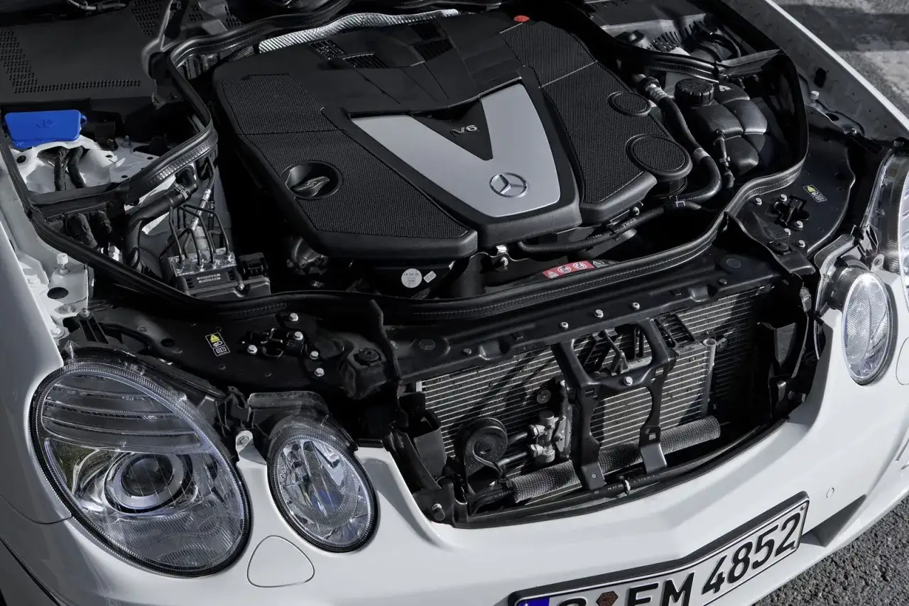 Silnik V6 w białym Mercedesie E500 W211, z widocznymi reflektorami i chłodnicą.
