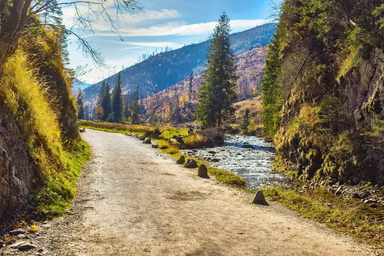Ścieżka w górach, idealna na hiking po polsku. Po prawej stronie szumi potok, po lewej skalne zbocze porośnięte trawami.