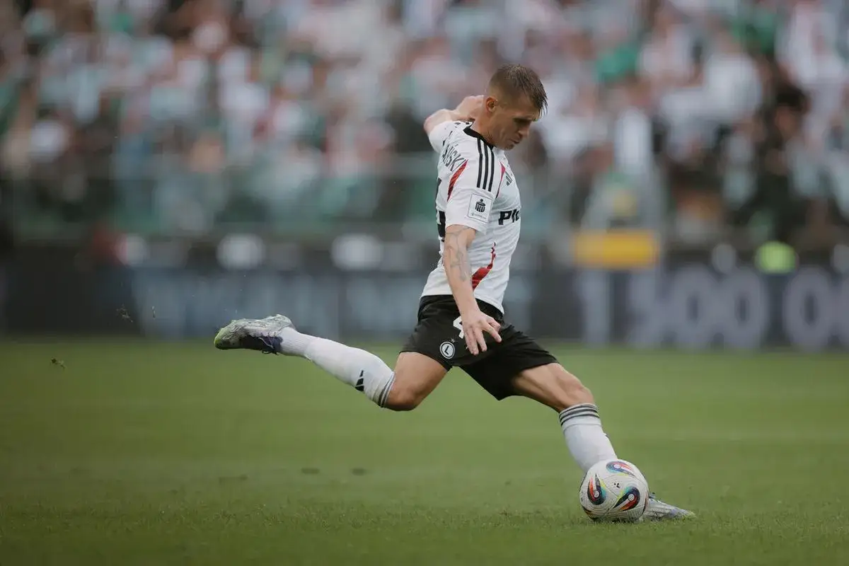 Piłkarz Legii Warszawa w akcji przeciwko Pogoni Szczecin. Dynamiczne uderzenie piłki na zielonej murawie stadionu.