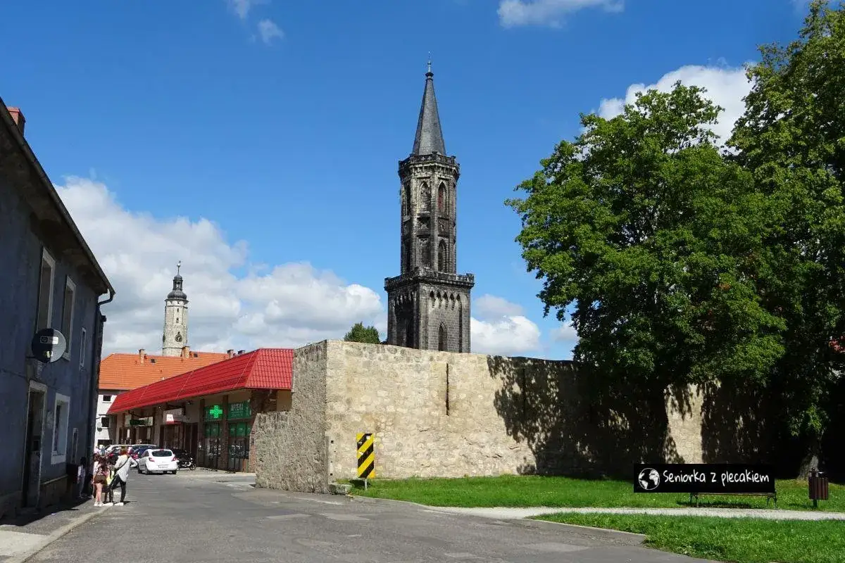 Wieża w Lw&oacute;wku Śląskim, jedna z gł&oacute;wnych atrakcji, g&oacute;ruje nad miastem. Obok niej mury obronne i zielone drzewa.