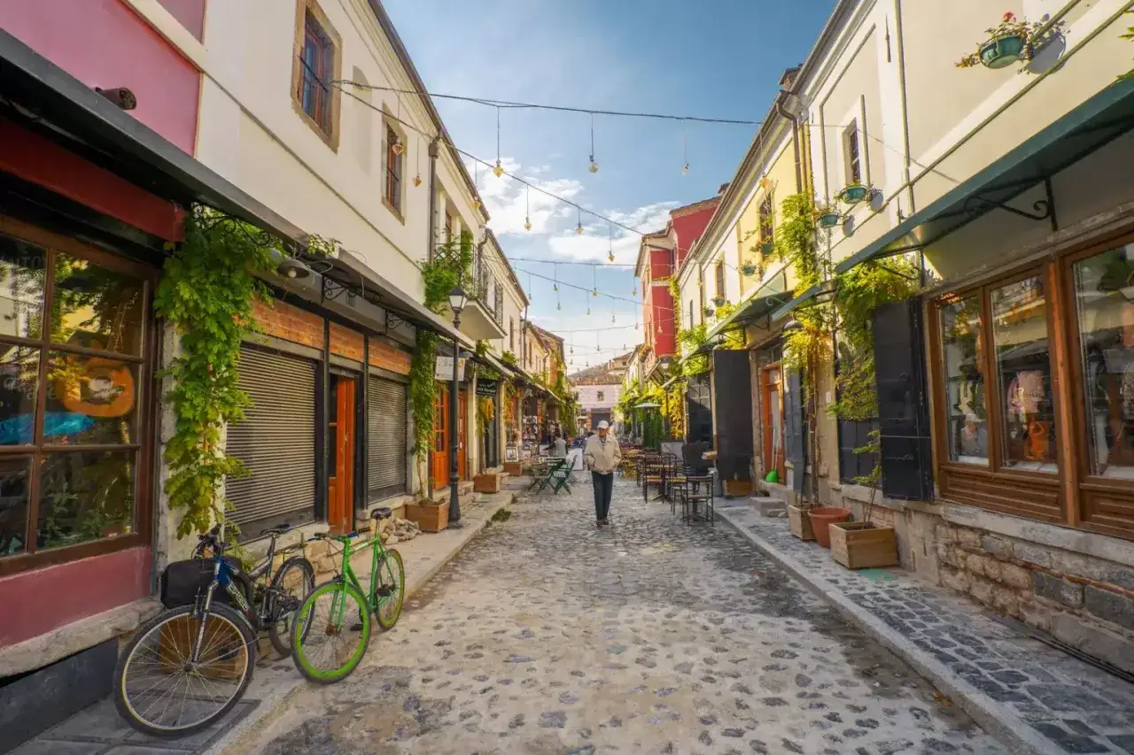 Urokliwa uliczka w Korce, Albania, z brukowaną nawierzchnią, kawiarnianymi stolikami i rowerami.