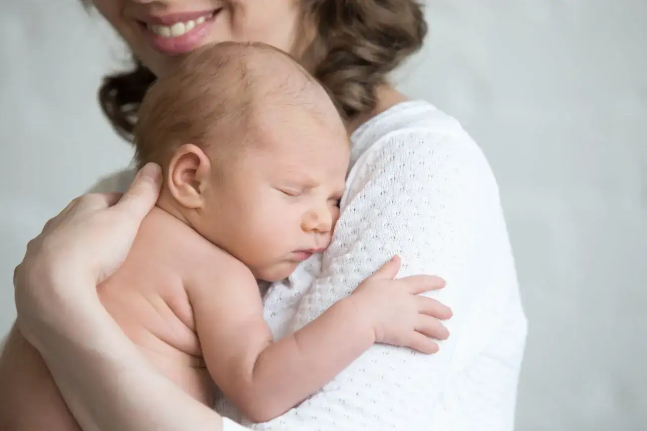 Uśmiechnięta mama tuli śpiące niemowlę. Warto wiedzieć, jaki lekarz wystawia zaświadczenie o karmieniu piersią.