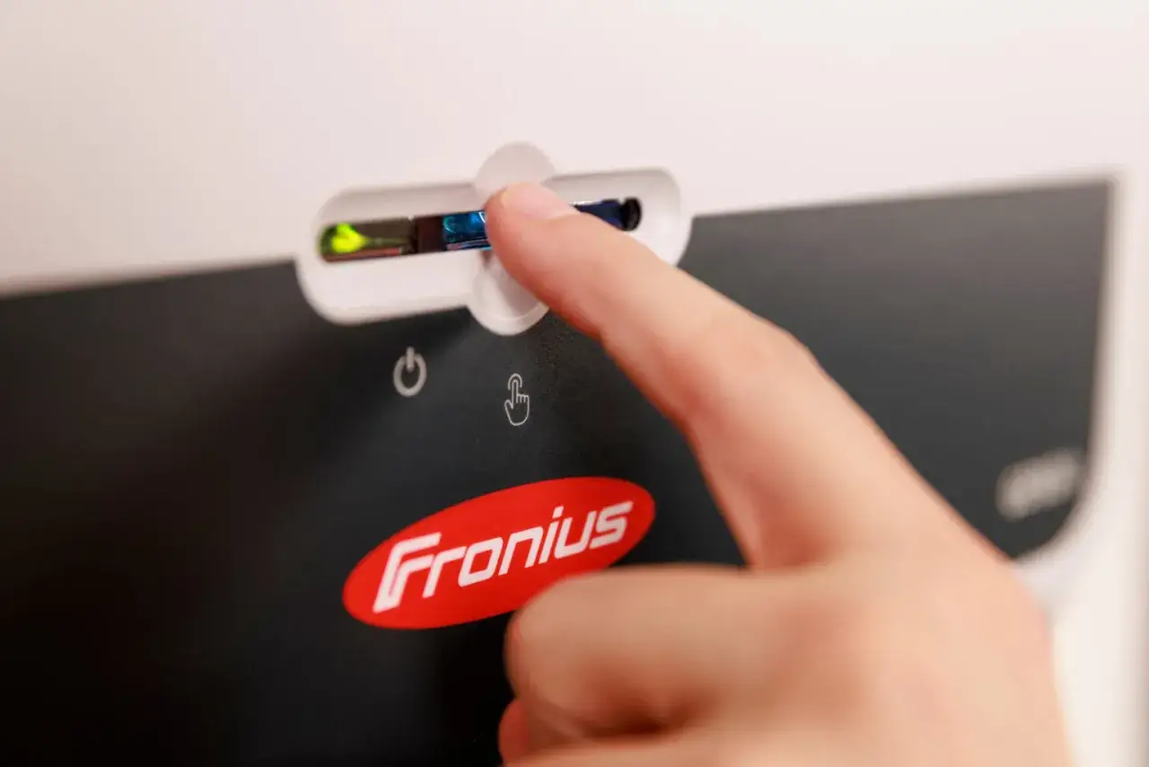 Palec dotyka przycisku na falowniku Fronius, aby połączyć go z Wi-Fi.