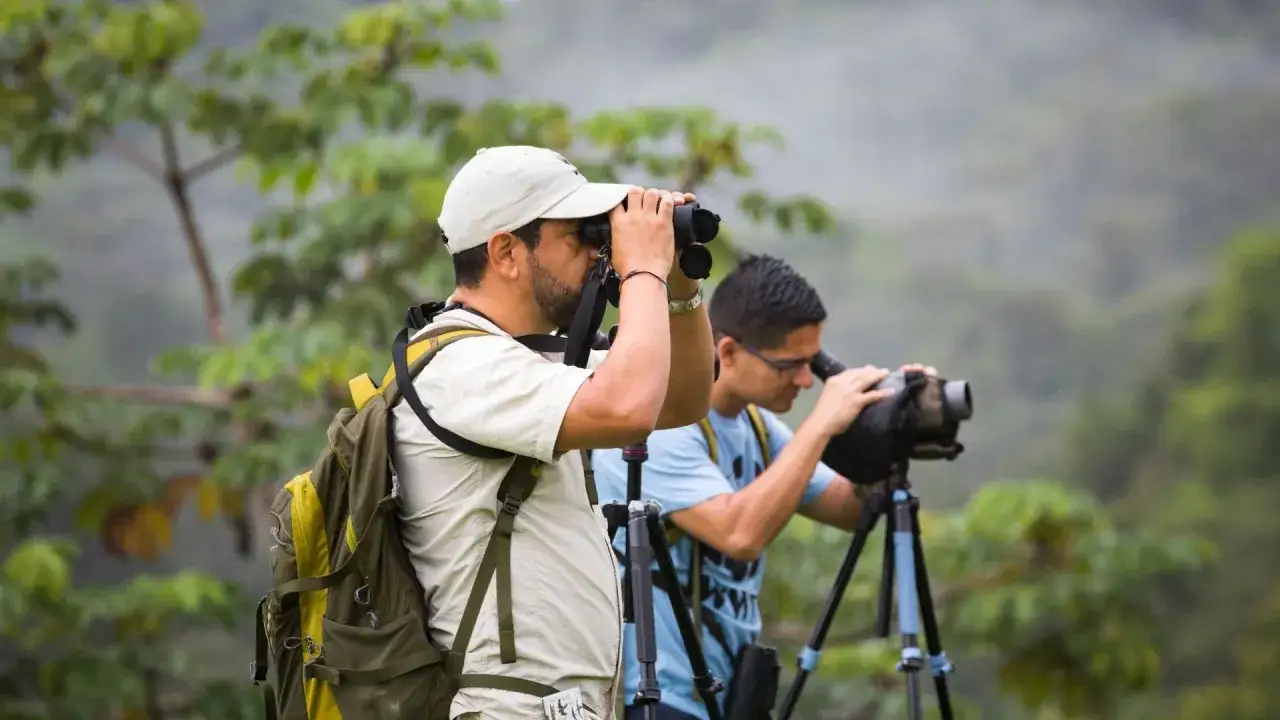 Dw&oacute;ch mężczyzn z plecakami obserwuje przyrodę przez lornetki i lunetę. To prawdziwy **outdoor**!