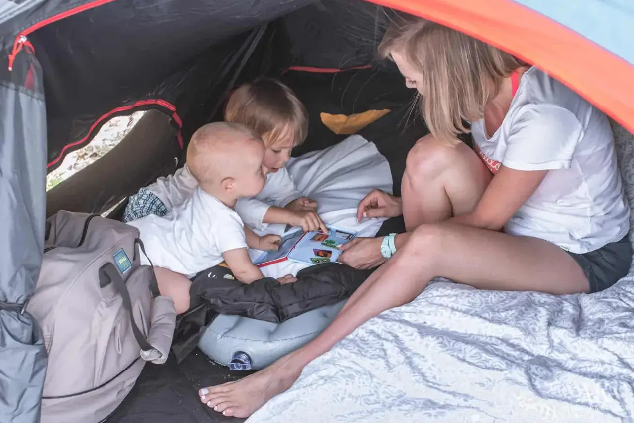 Mama z dwójką dzieci czyta książeczkę w namiocie. To świetny pomysł, co zabrać pod namiot z dziećmi, by zapewnić im rozrywkę.