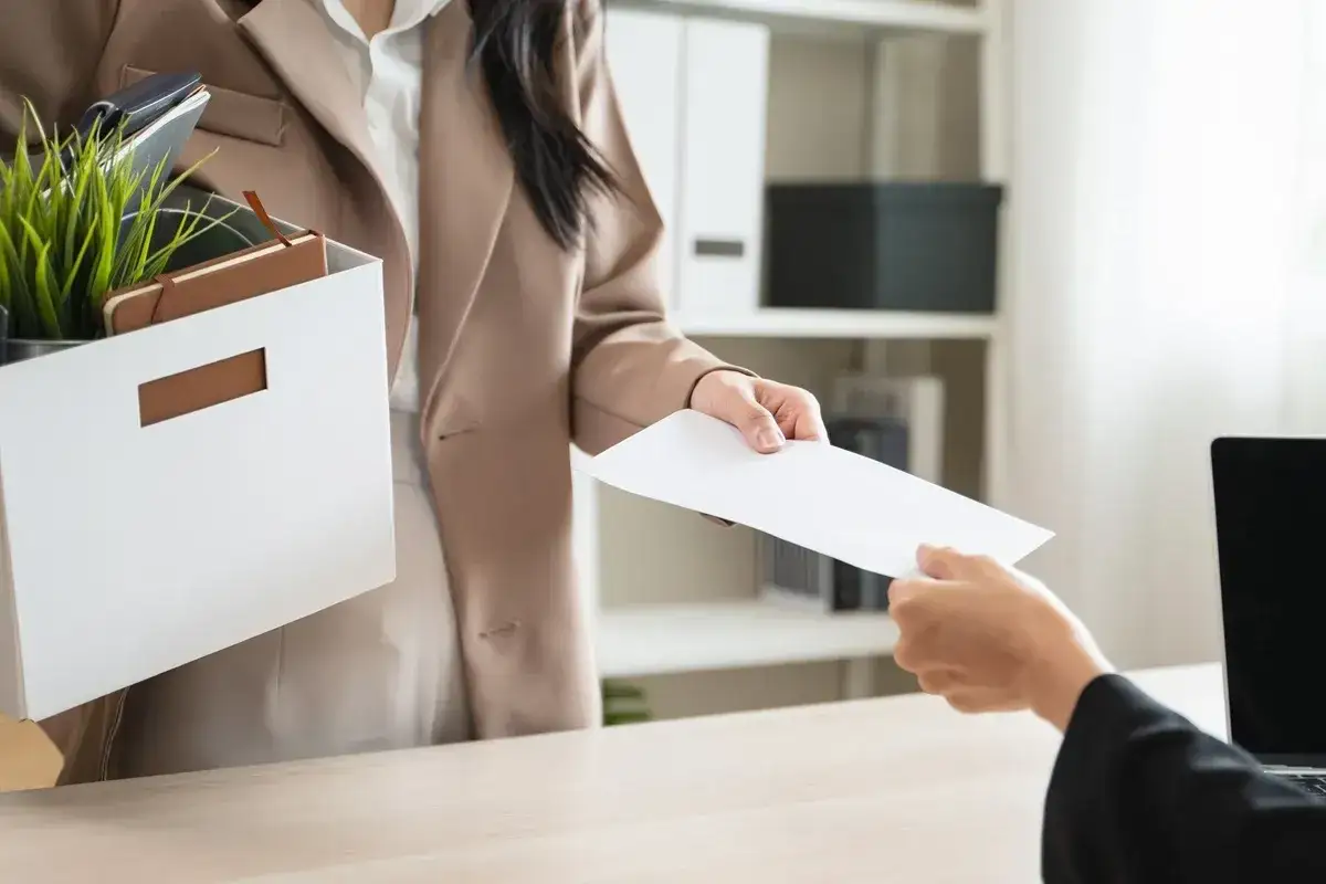 Kobieta z pudełkiem osobistych rzeczy przekazuje dokumenty, symbolizując rezygnację ze stanowiska kierowniczego.
