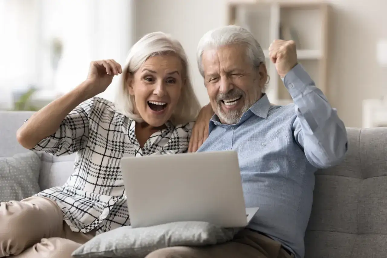 Szczęśliwa para seniorów odkrywa, czy praca na emeryturze zwiększa emeryturę, ciesząc się wynikami na laptopie.