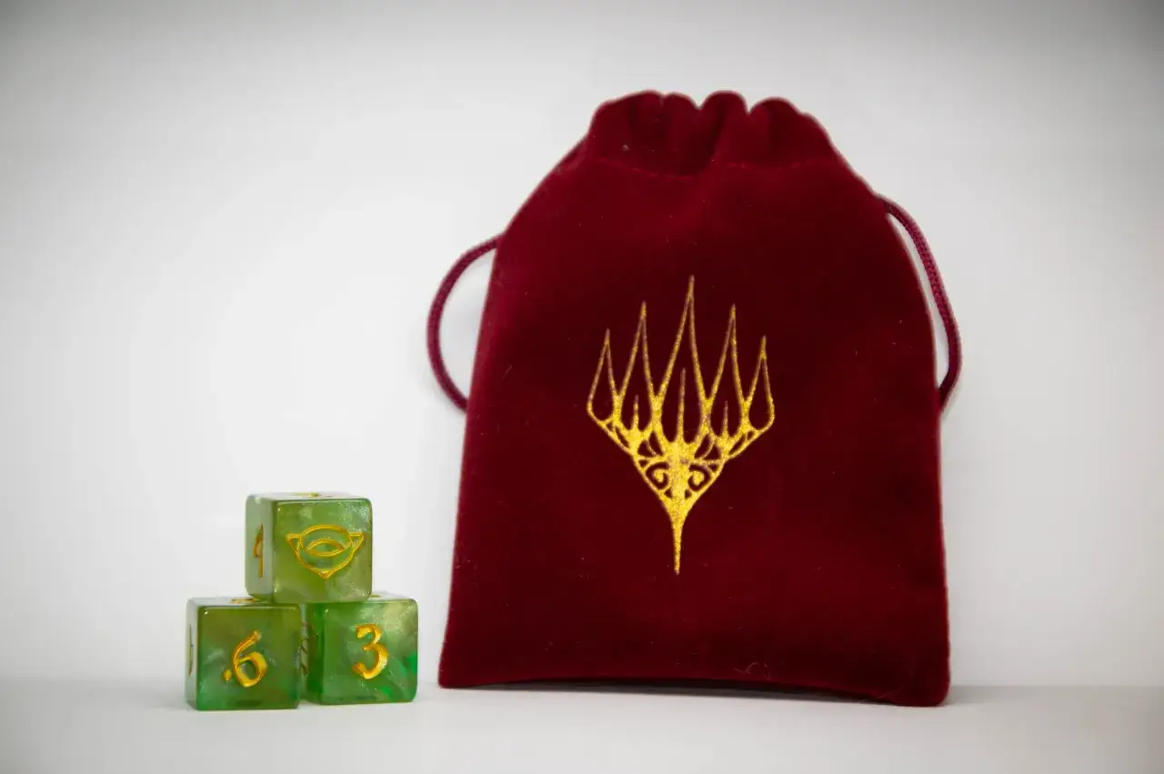 Czerwony woreczek z logo Wizards of the Coast MTG i zielone kostki do gry.