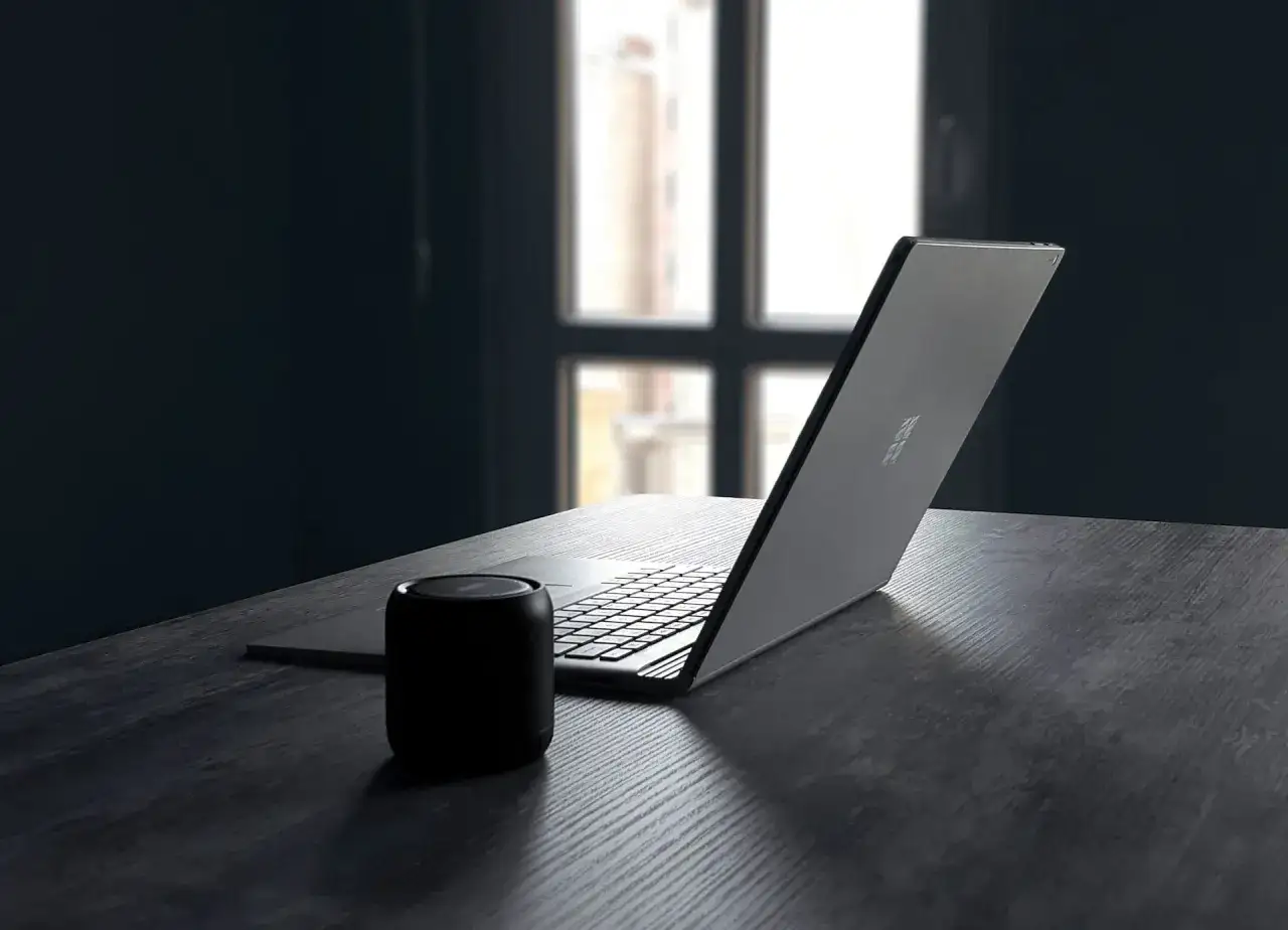 Czarny głośnik bluetooth obok otwartego laptopa na drewnianym biurku. Proste kroki, jak podłączyć głośnik bluetooth z laptopem.