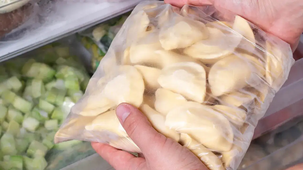Ręce trzymają worek z zamrożonymi pierogami, gotowymi do przechowywania. To prosty sposób, jak mrozić pierogi, by cieszyć się nimi później.