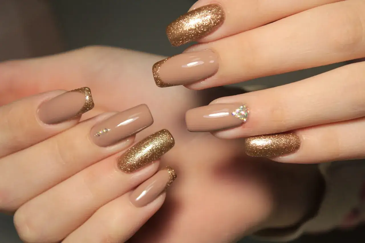Eleganckie paznokcie w kolorze beżowym z brokatowym french manicure i subtelnymi cyrkoniami.