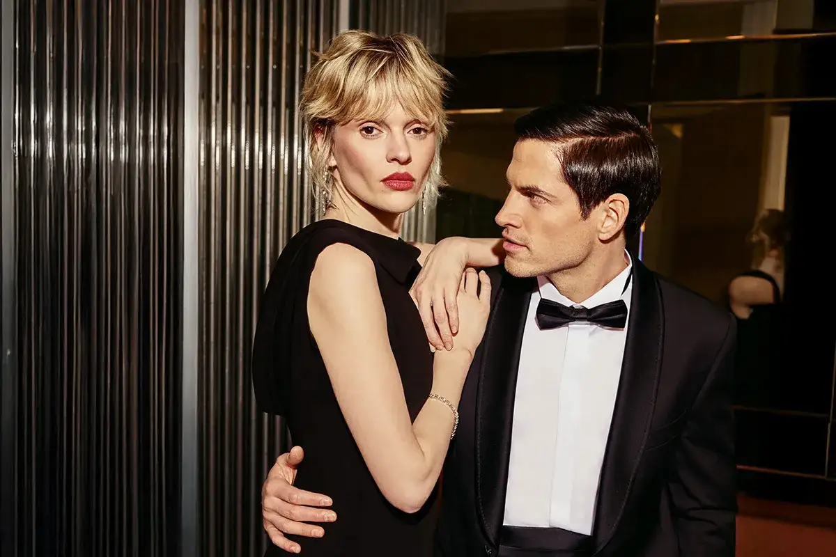 Elegancka para, on w smokingu, ona w czarnej sukni. Idealny przykład, jak się ubrać do teatru, by zrobić wrażenie.