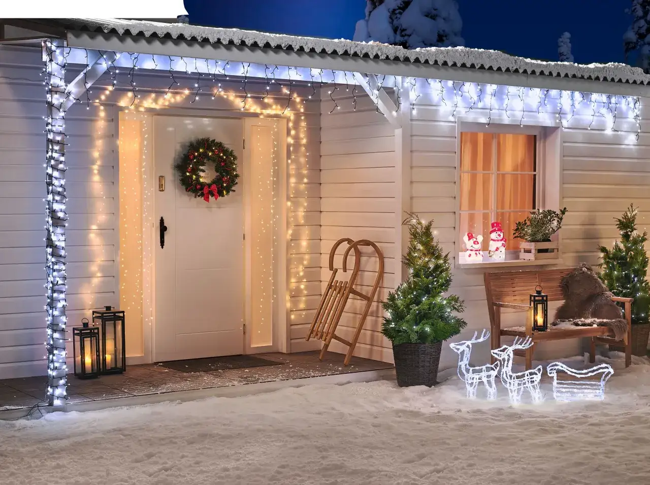 Magiczna aranżacja drzwi wejściowych w zimowej scenerii. Śnieg, choinki i renifery z sanie tworzą świąteczny nastrój.