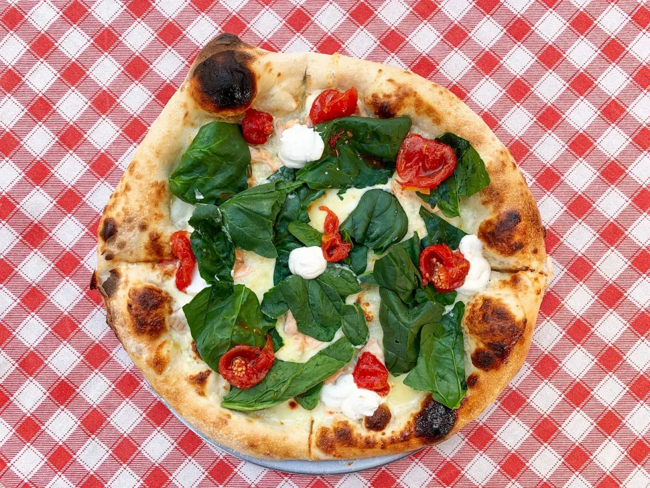 Pyszna pizza ze szpinakiem i pomidorkami na czerwono-białym obrusie. Zastanawiasz się, ile kosztuje pizza we Włoszech?